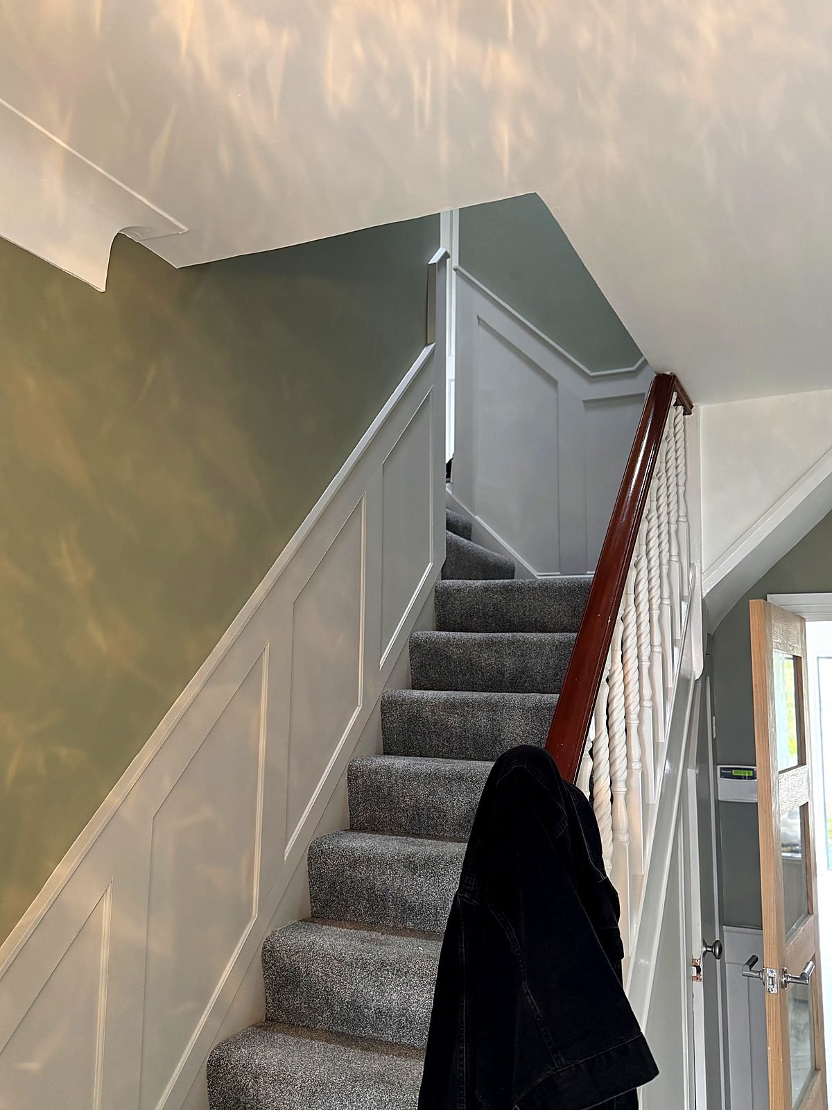 Hallway and staircase wall panelling, painted in soft white against a sage green wall